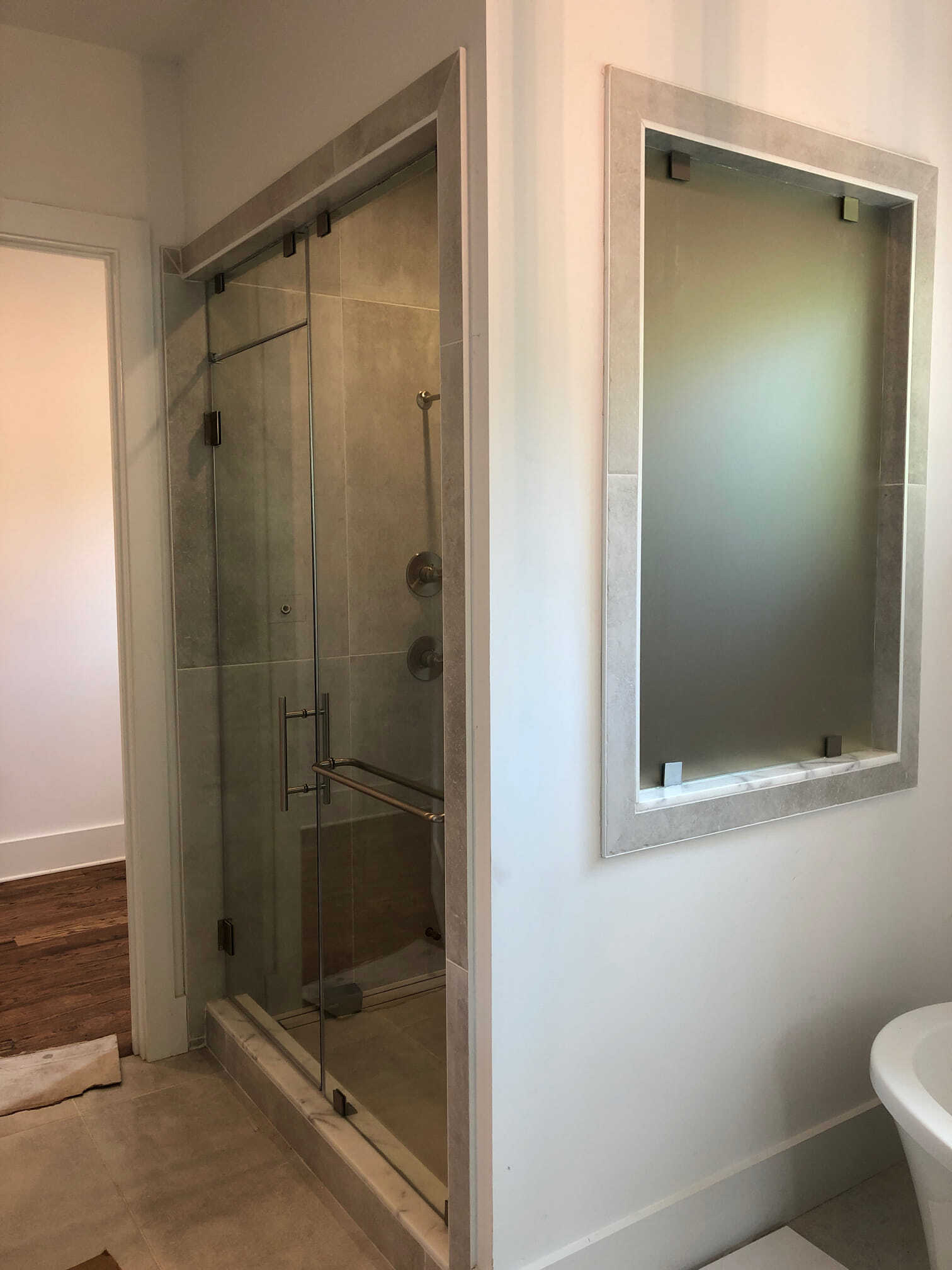 Shower with glass door, bench, and frosted window in a bathroom. Light tile and white walls.