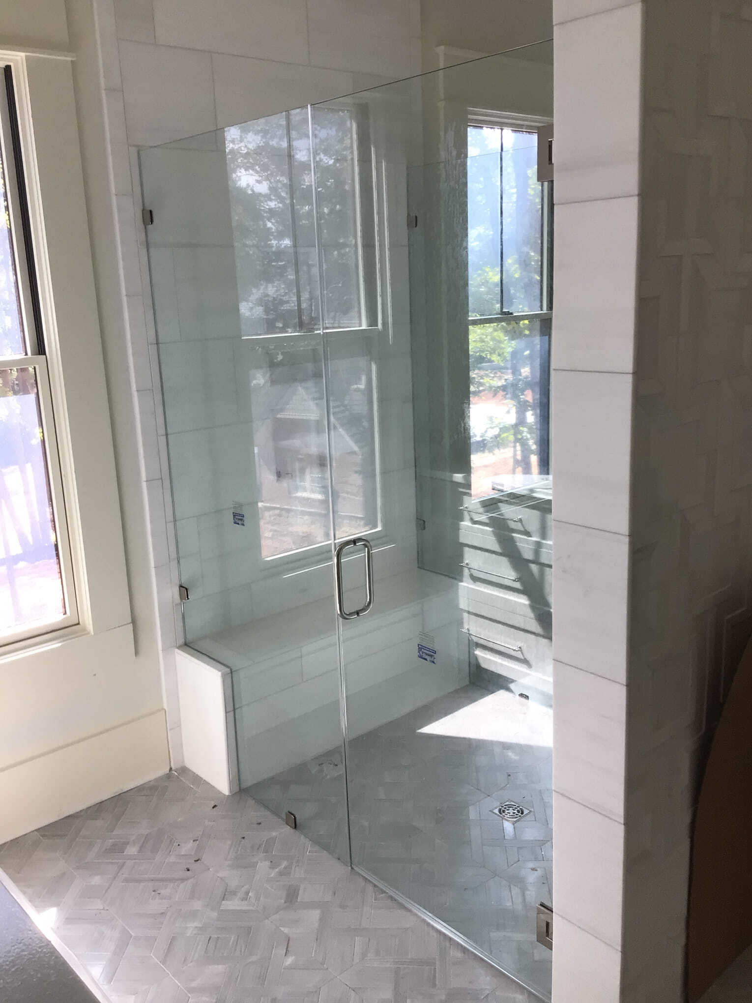 Glass shower enclosure with a seat, next to a window, in a bathroom with white tile.