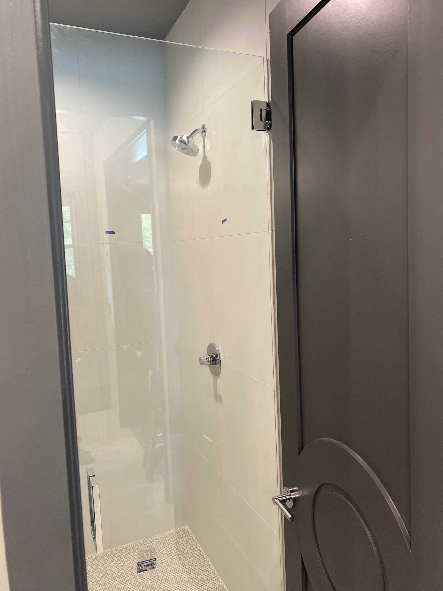 Glass shower enclosure with gray door and white tiled walls. Chrome shower fixtures.