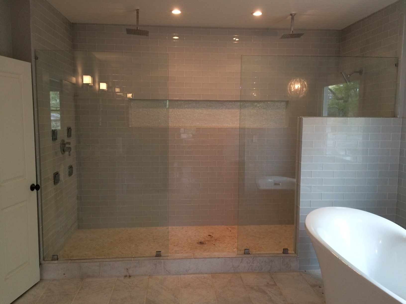 Spacious bathroom with glass shower enclosure, two shower heads, and a freestanding white bathtub.