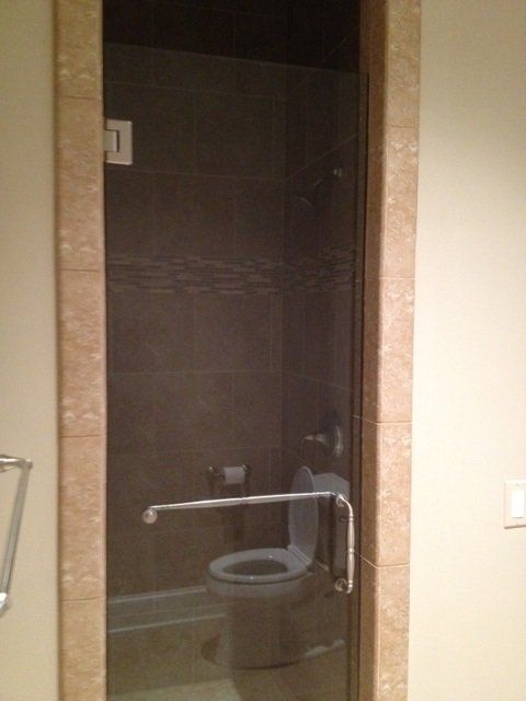 Glass shower door with a toilet inside, bordered by light-colored tile.