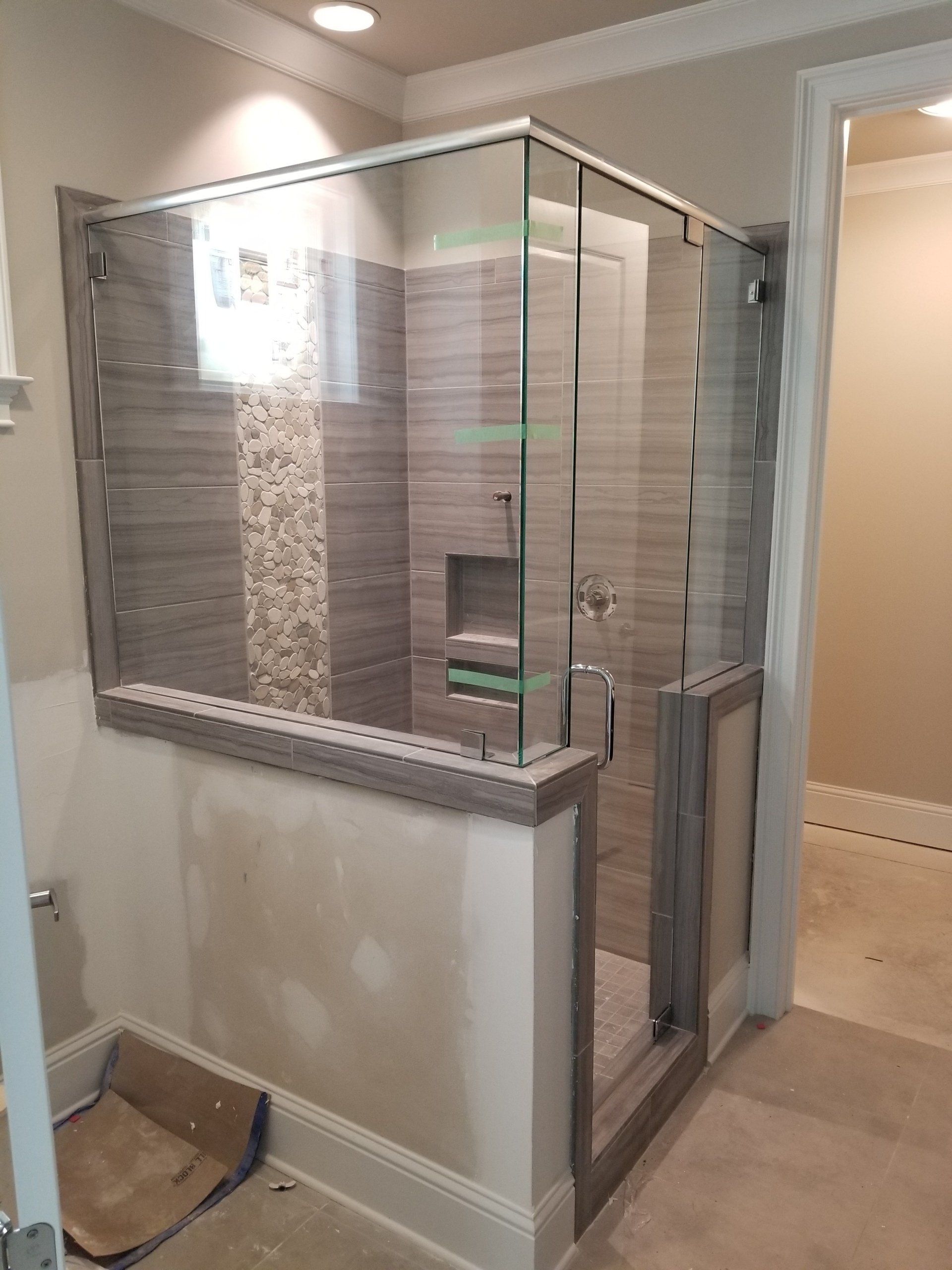 Glass shower enclosure with gray tile and pebble accent; bathroom under construction.