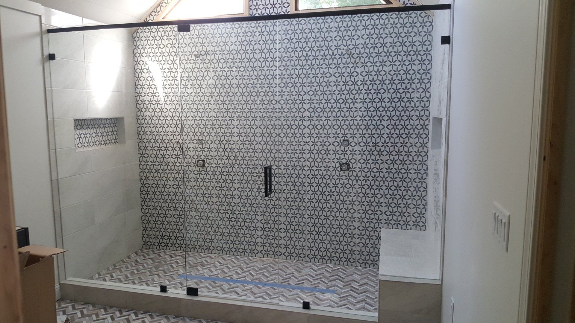 Shower with clear glass doors, black trim, and patterned tile walls and floor.