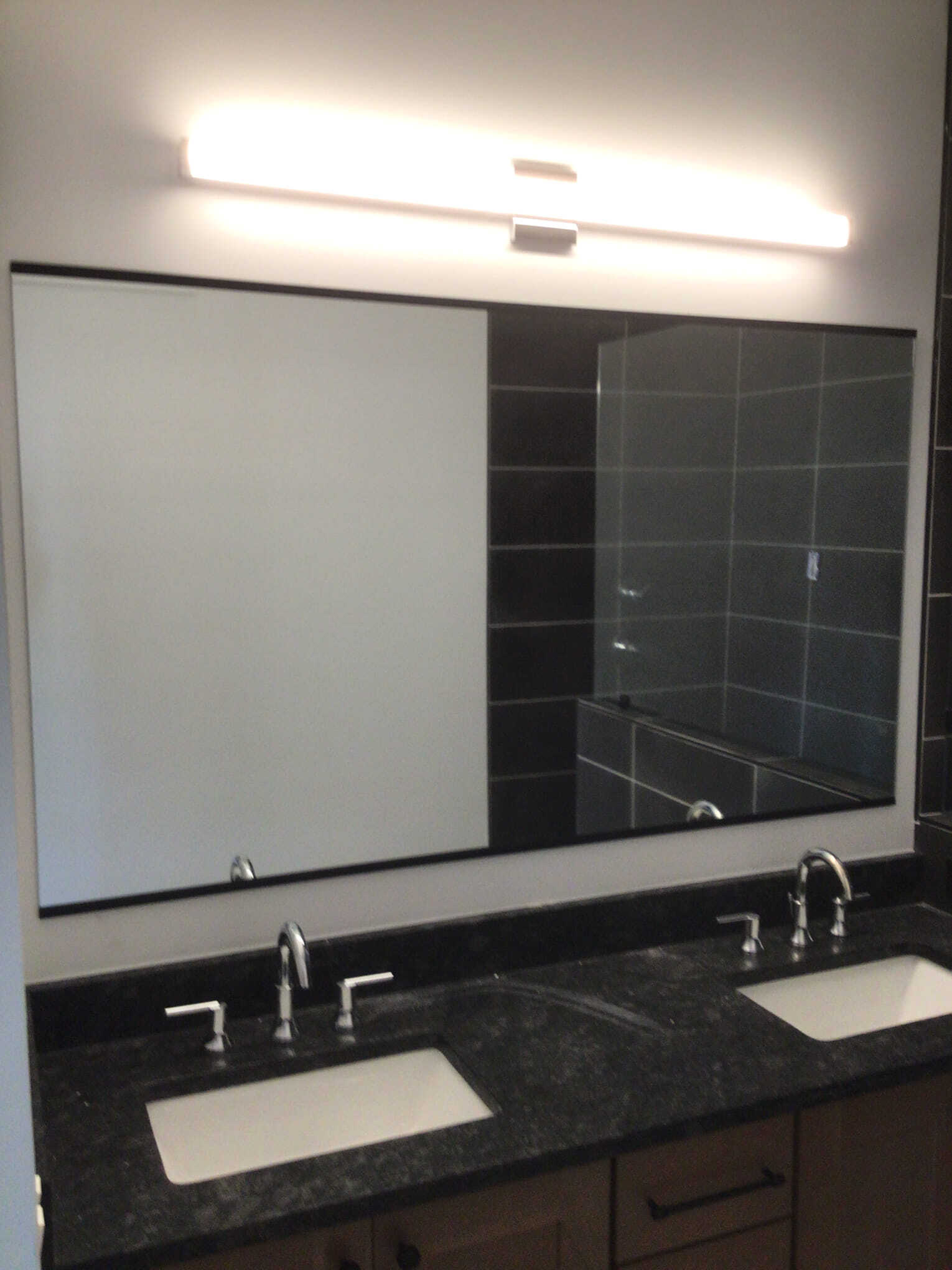 Bathroom with dual sinks, large mirror, black granite countertop, and linear light fixture.