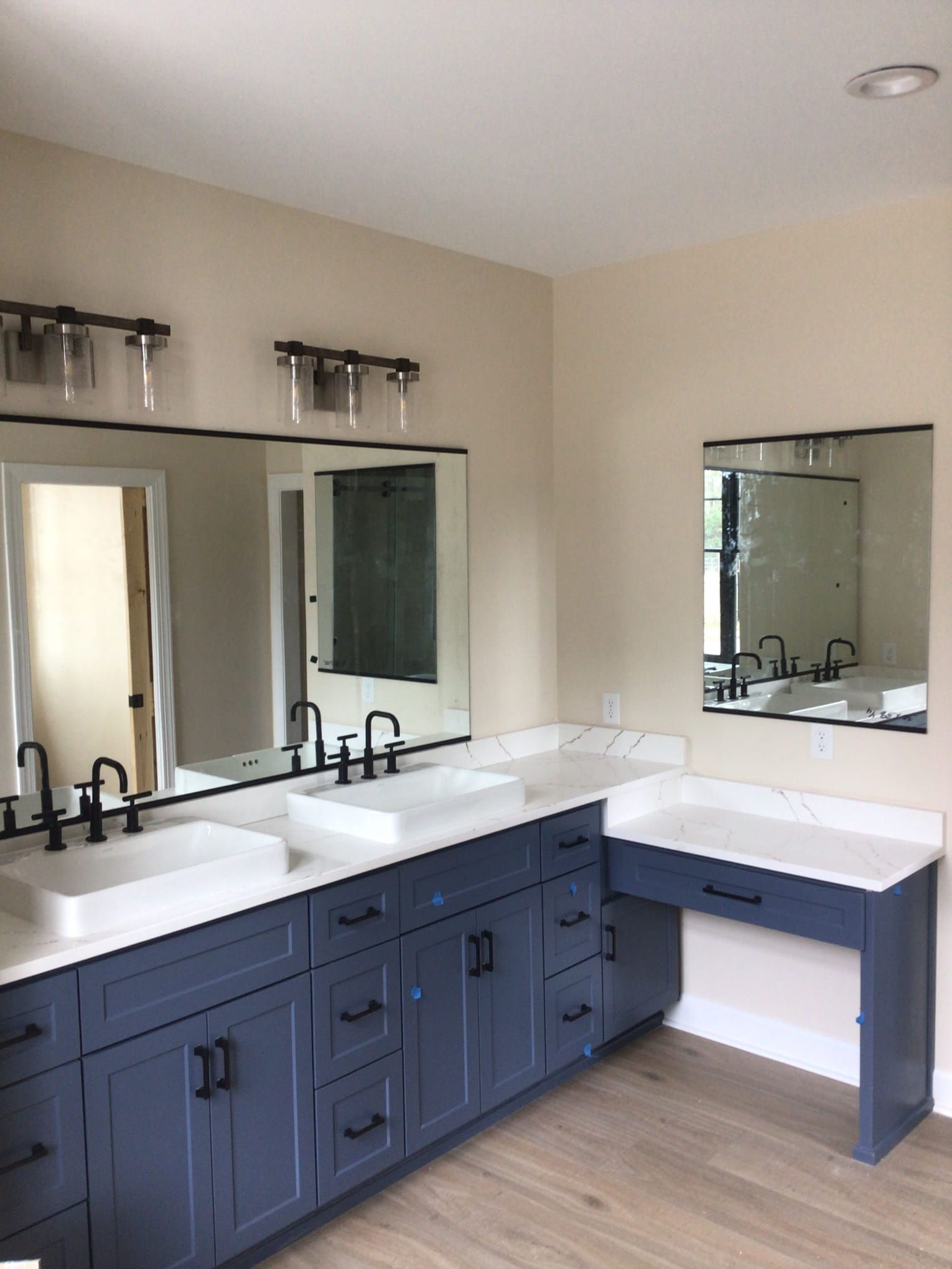 Blue bathroom vanity with white countertop, sinks, and mirrors. Dark hardware and light fixtures.