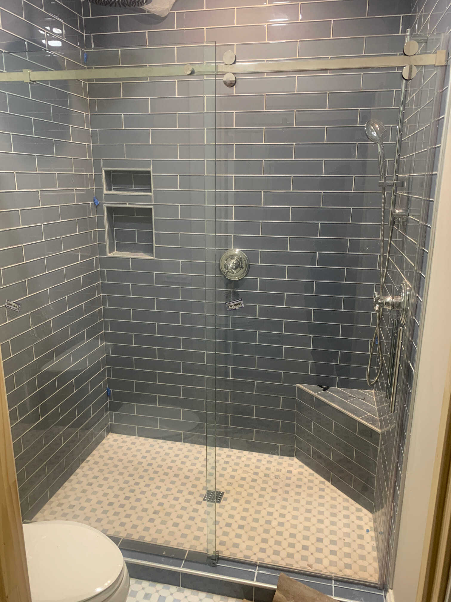 Modern shower with blue brick tiles, glass door, and white and gray mosaic floor.