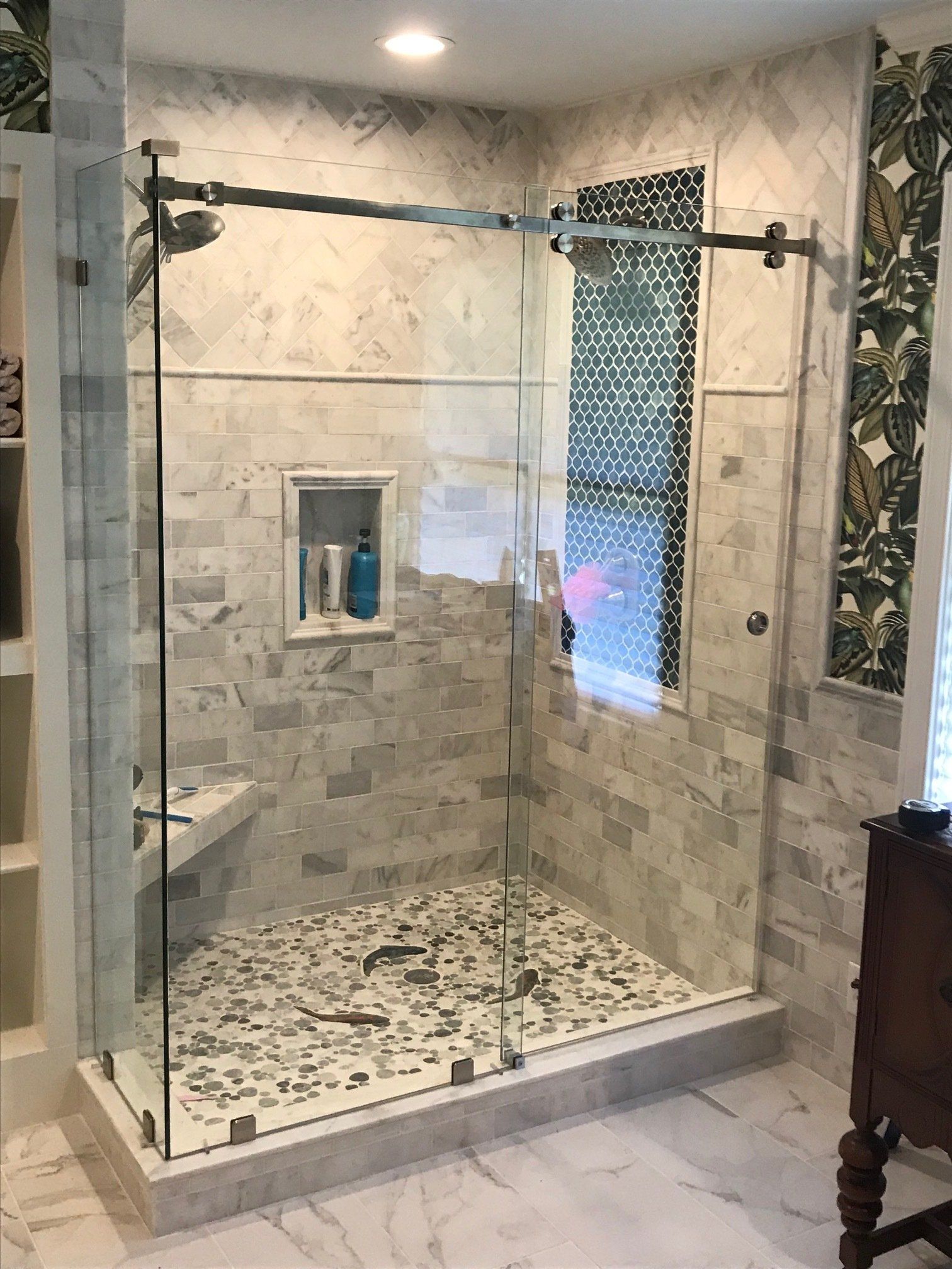 Glass shower enclosure with gray and white tile, shower head, and stone floor.