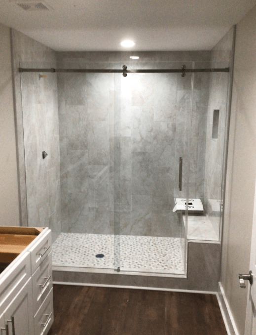 Shower with gray tiled walls, glass door, built-in seat, pebble floor, and sliding door hardware.