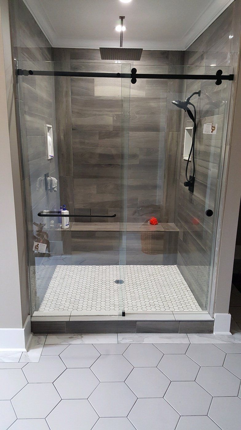 Modern shower with glass door, stone floor, built-in bench, dark fixtures, and wood-look tiled walls.
