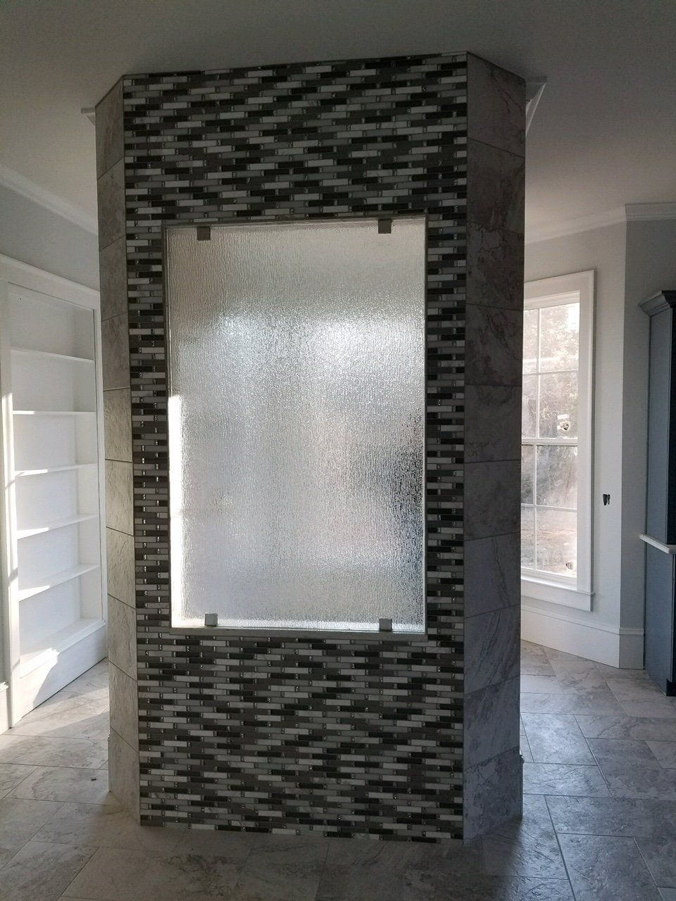 Shower enclosure with decorative mosaic tile, textured glass panel, and light-colored tile floors.
