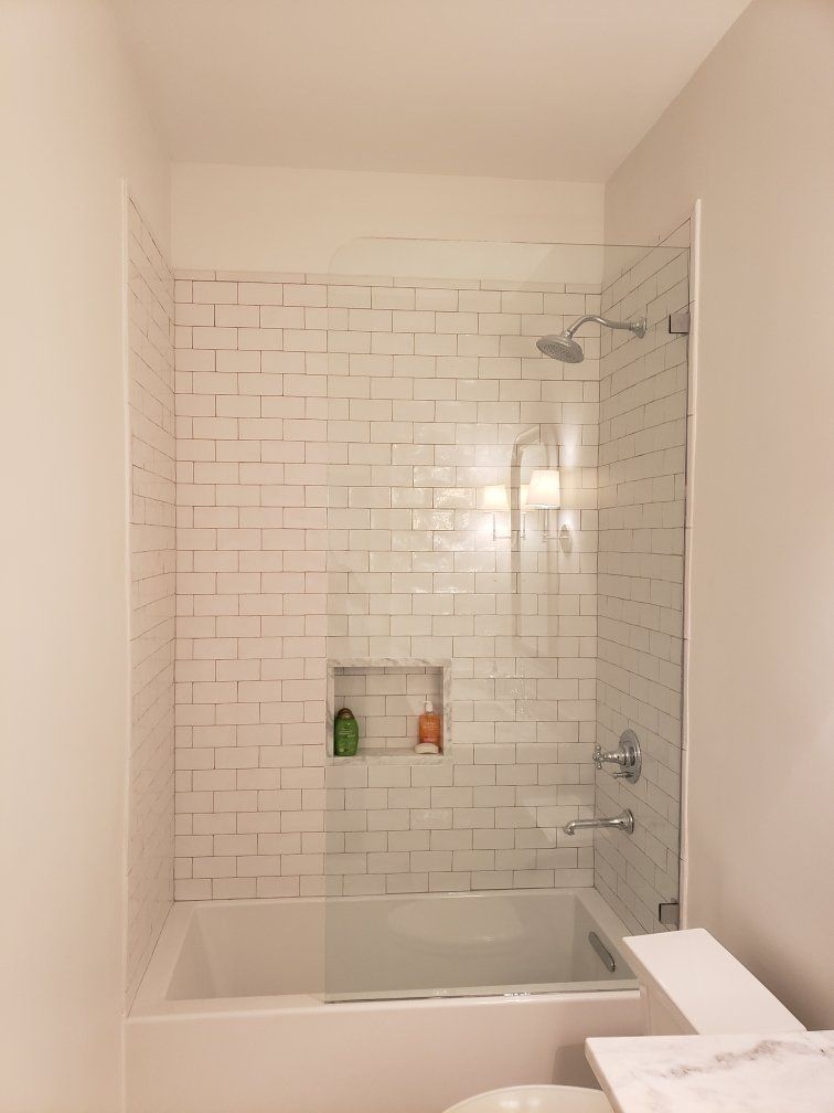 White-tiled shower with glass door and built-in shelf; chrome fixtures.
