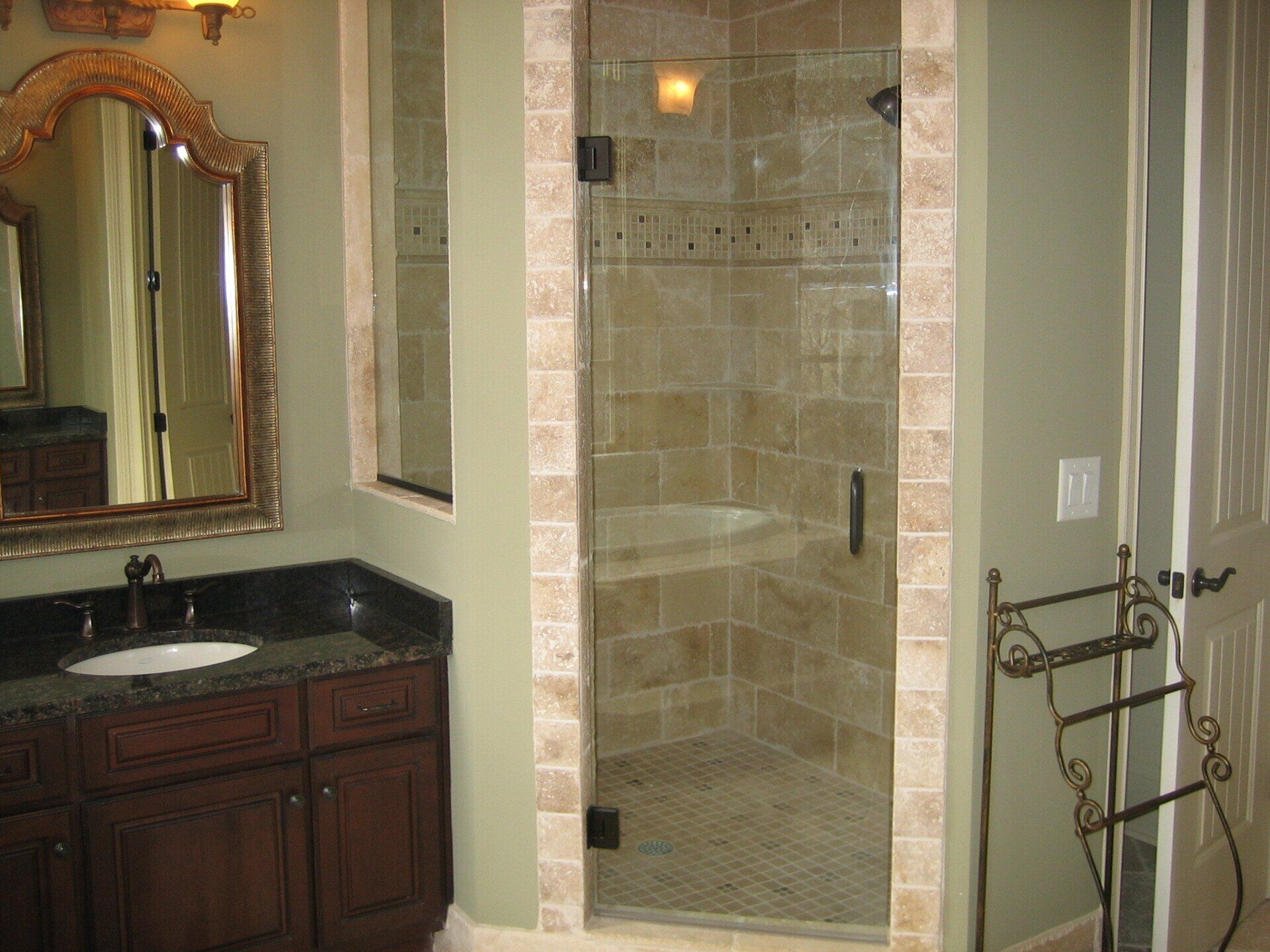 Bathroom with dark wood vanity, stone shower with glass door, and ornate mirror.