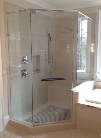 Glass-enclosed, tiled shower with silver fixtures, corner shape, and small gray floor tiles.