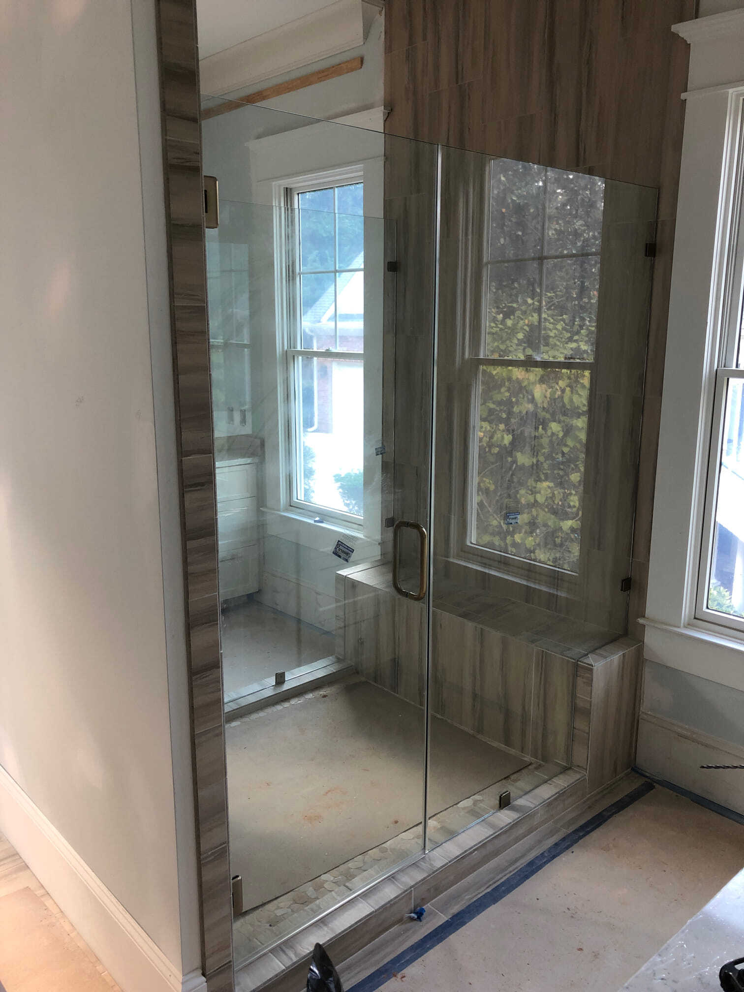 Glass-enclosed shower with a door, wood-look tiled walls, and a window.