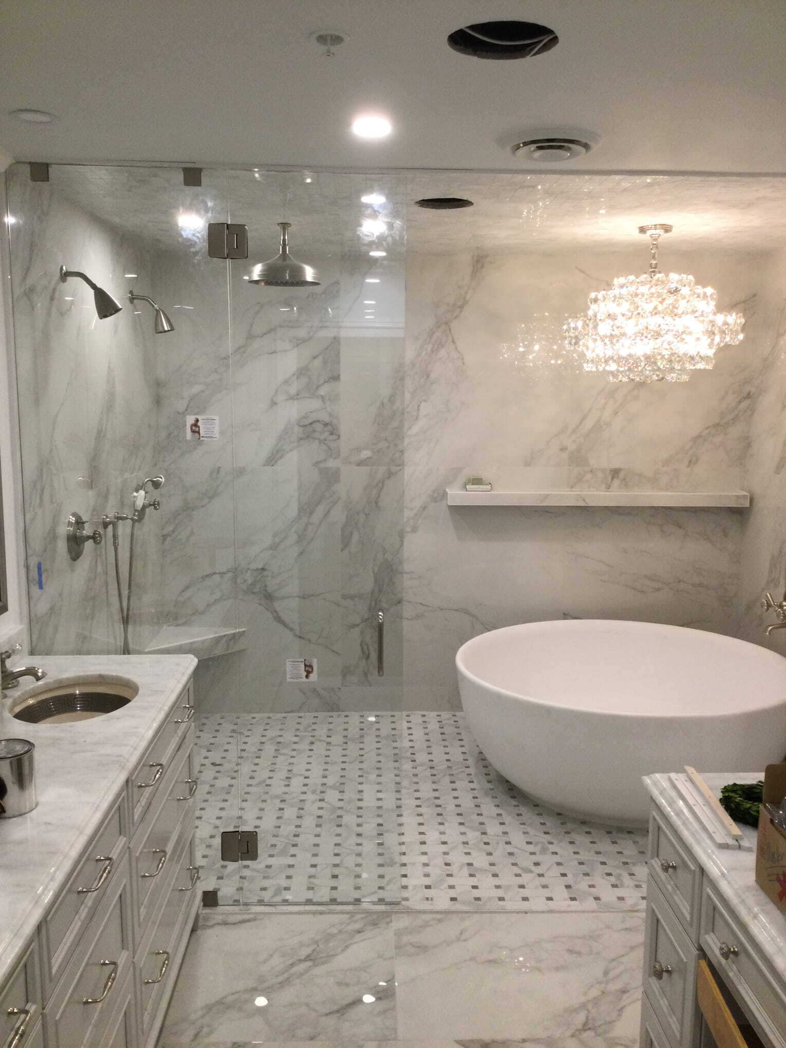 Luxurious bathroom with marble walls and floors, a glass shower, a soaking tub, and a chandelier.