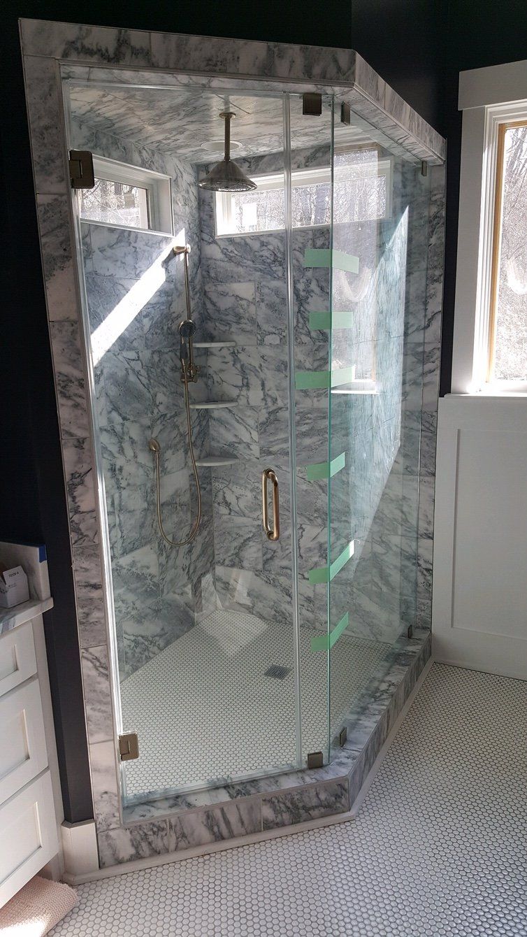 Marble-tiled shower with glass doors and a square shower head, set on a mosaic-tiled floor.