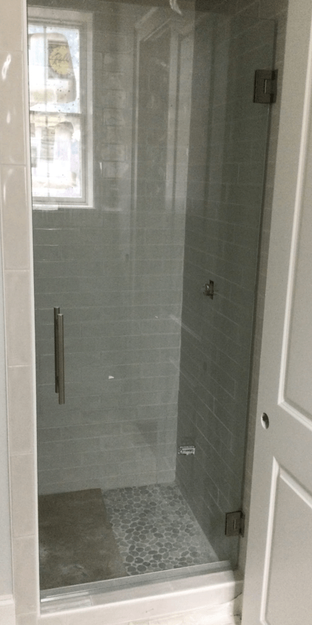 A walk-in shower with a glass door, light gray tile, and a small window.