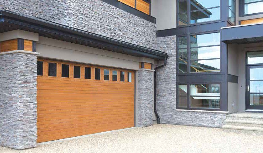 Garage door of a modern house, with stone and wood accents. Brown garage door, gray stone exterior.