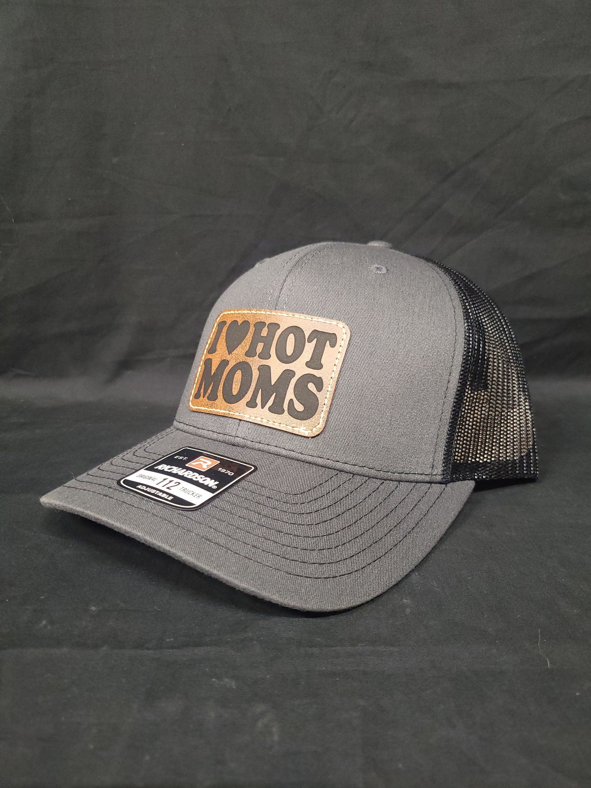 A gray hat with a leather patch that says `` i love hot moms '' is sitting on a black surface.