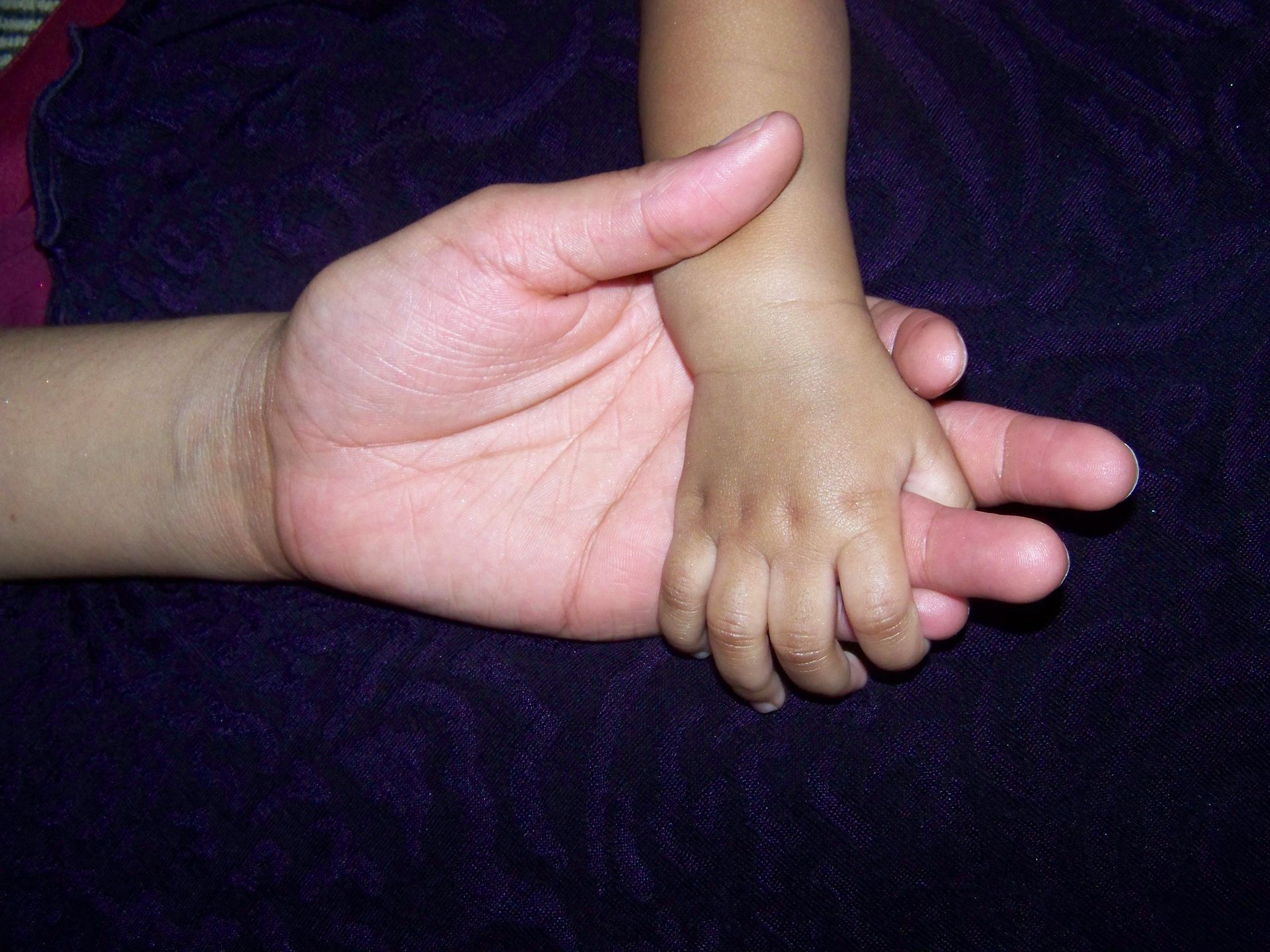 Adult hand holding a baby's foot on a dark purple blanket