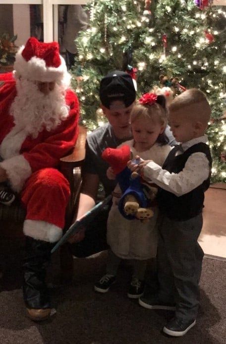 Santa sitting with three children by a decorated Christmas tree, sharing a holiday gift
