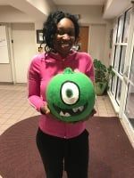 Person in a pink top holding a green cartoon monster plush in a hallway.