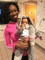 Woman in pink top holding a baby in a gray outfit indoors near a doorway.