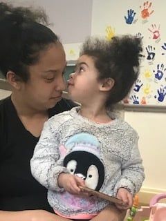 Woman and child facing each other indoors, with a penguin shirt and colorful handprints on the wall.