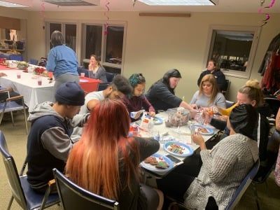 People gathered around a table in a bright room, eating and talking during a casual meal.