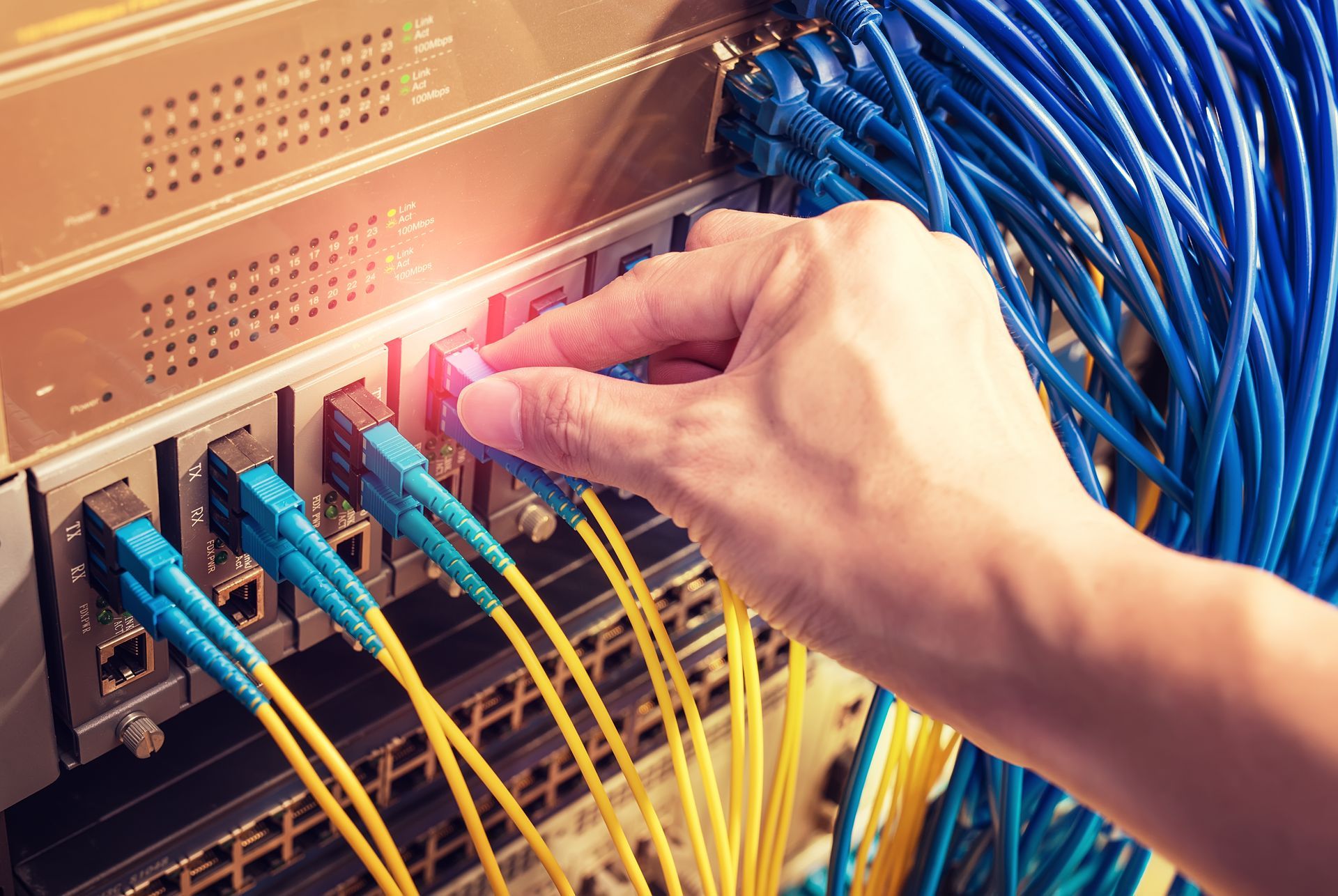 A person is plugging a fiber optic cable into a switch.