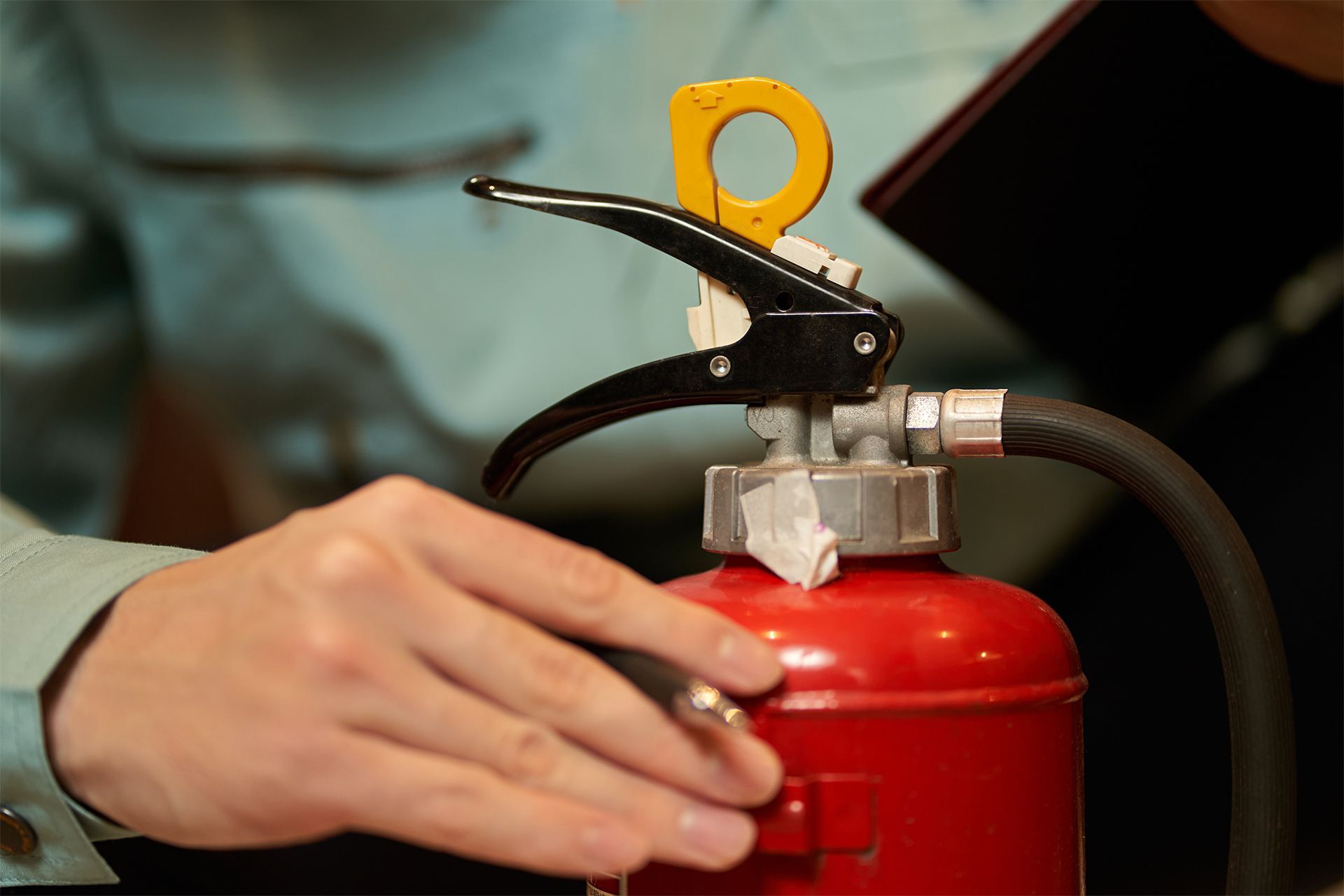 Person's hand pulling a pin from a red fire extinguisher, preparing to use it.