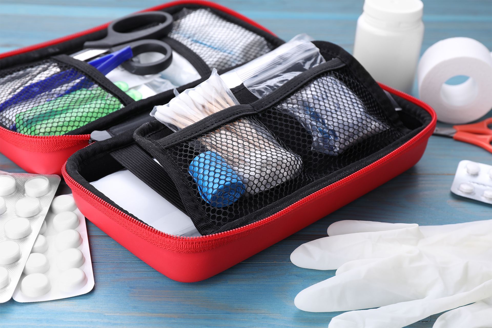 Red first aid kit open on a blue surface, with medical supplies like bandages and pills.