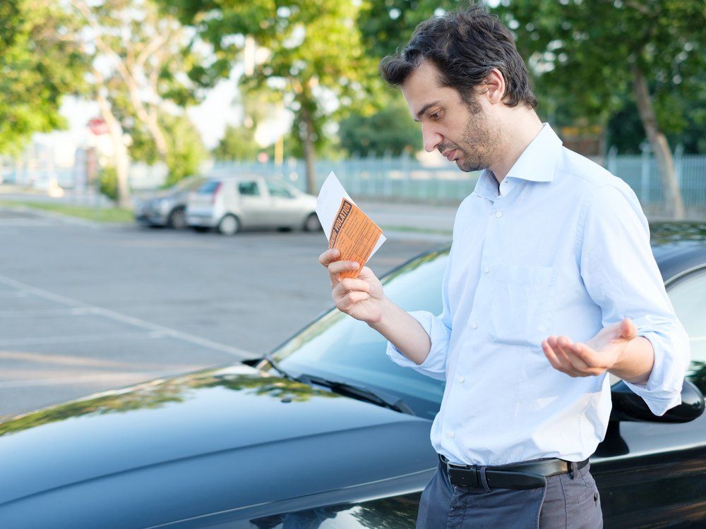 Un homme se tient à côté d'une voiture et tient un morceau de papier.