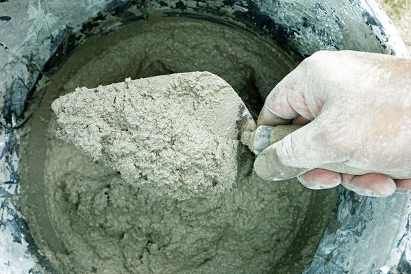 A person is mixing concrete in a bucket with a trowel.