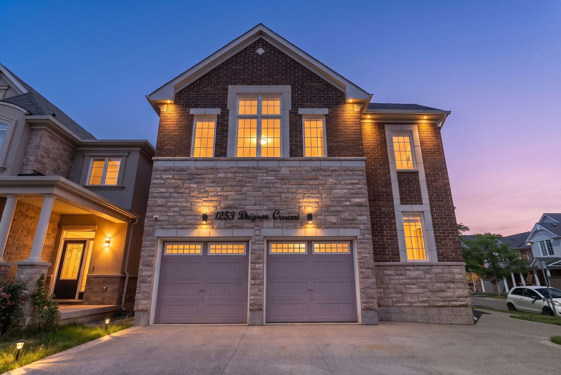 Luxury stone house at dusk with warm lit windows and a two-car garage