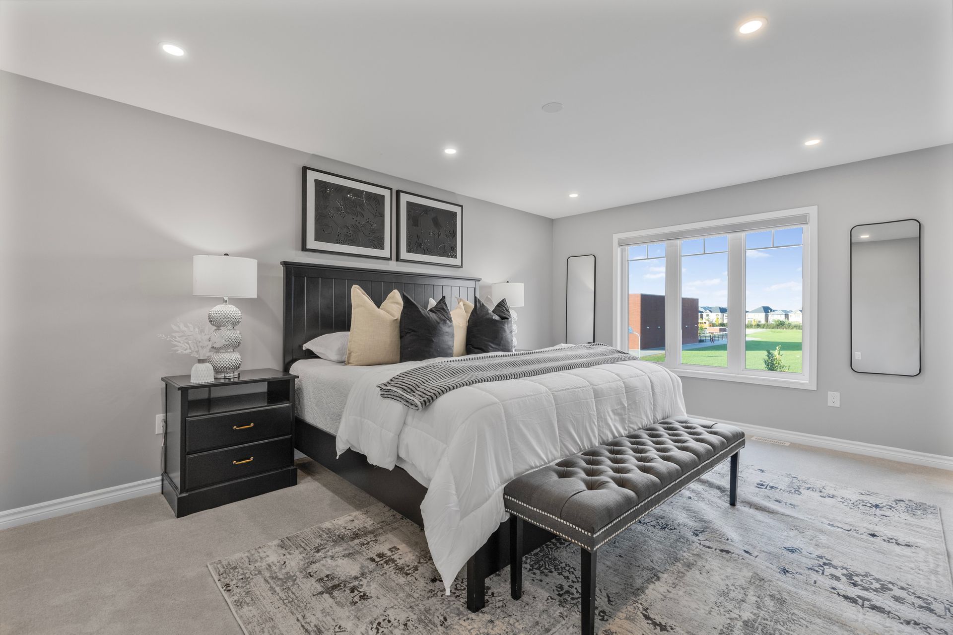 Bright modern bedroom with a large bed, bench, nightstand, and window overlooking a grassy yard.