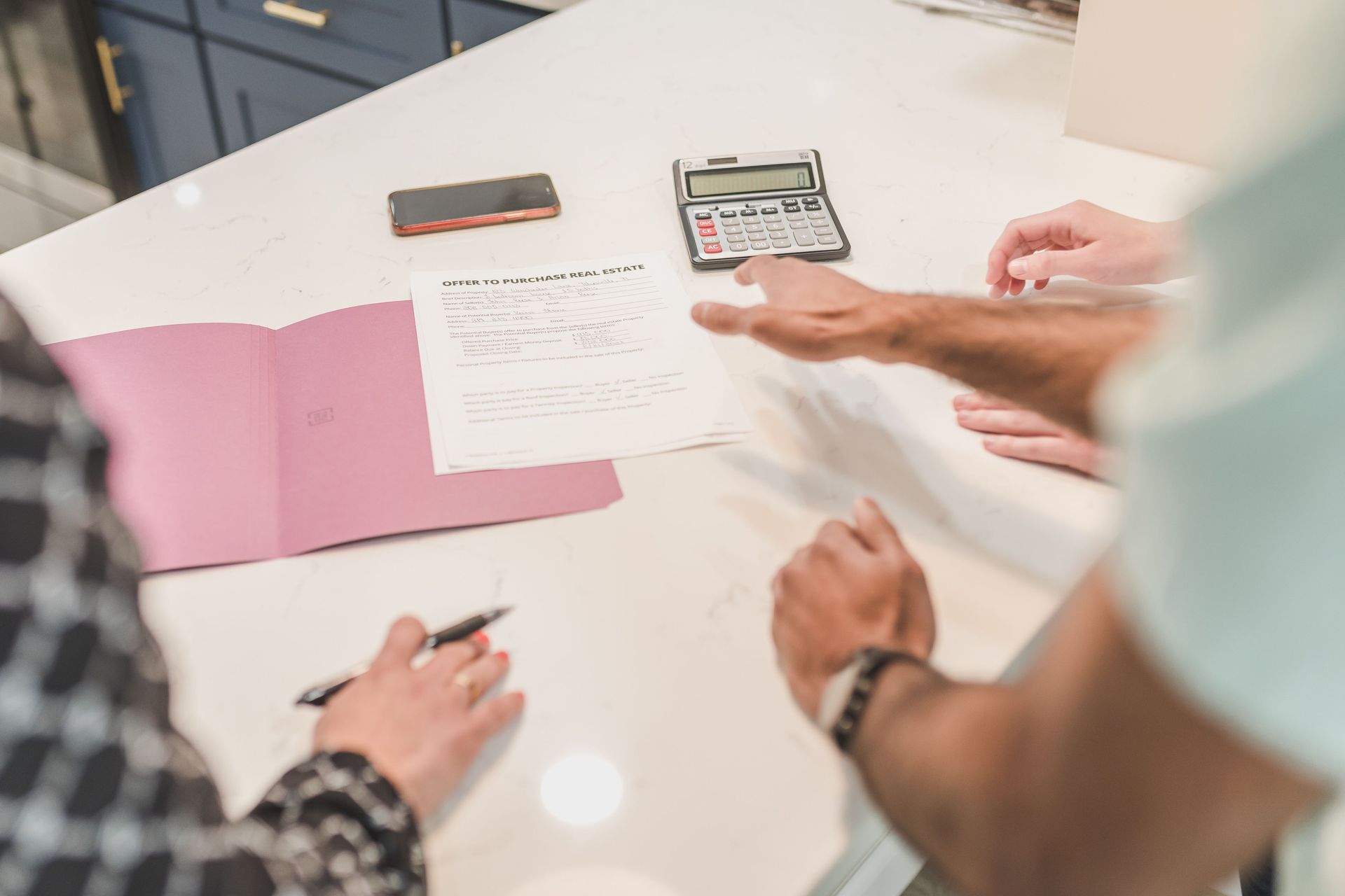 Hands reviewing documents and a calculator on a white desk with pink folders