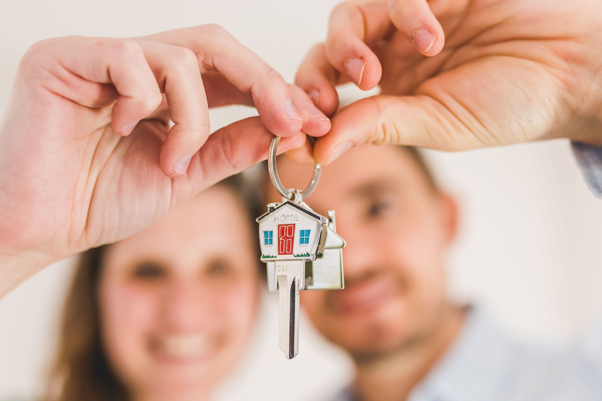 Hand holding a keychain in front of a blurred real estate sign reading “SOLD” and “SECH.”