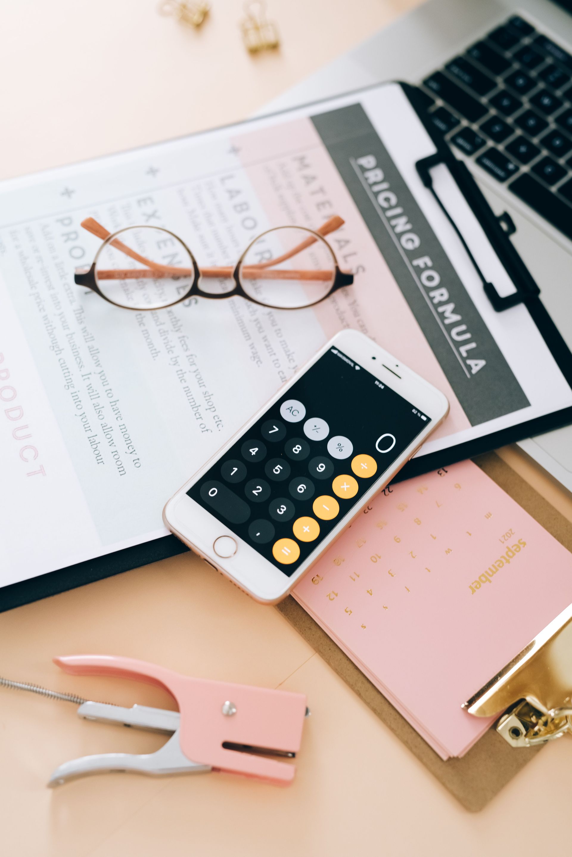 Desk with calculator, glasses, notebook, ruler, and pink stationery for budgeting or accounting
