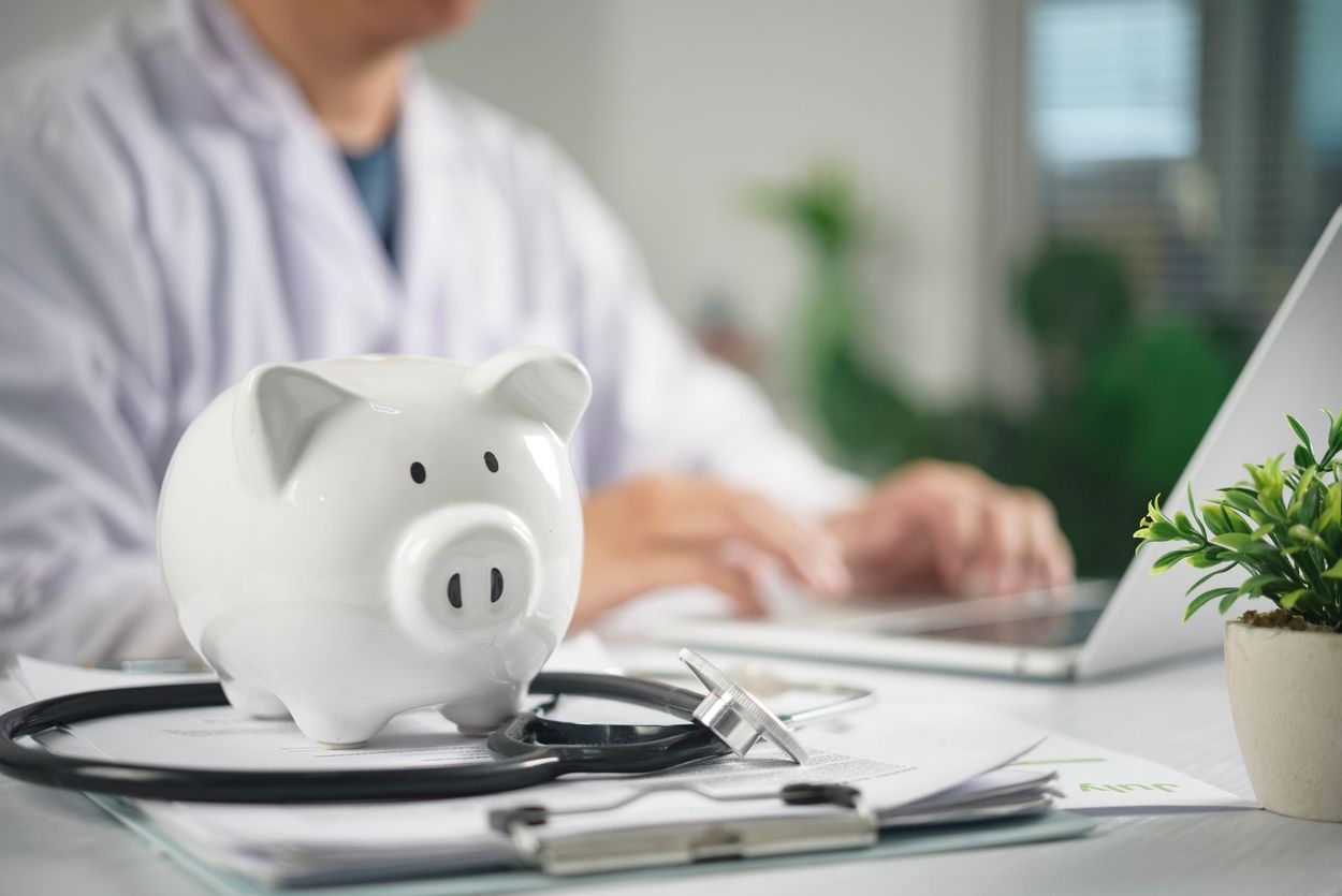 Piggy bank with stethoscope on a desk beside a laptop in a medical office