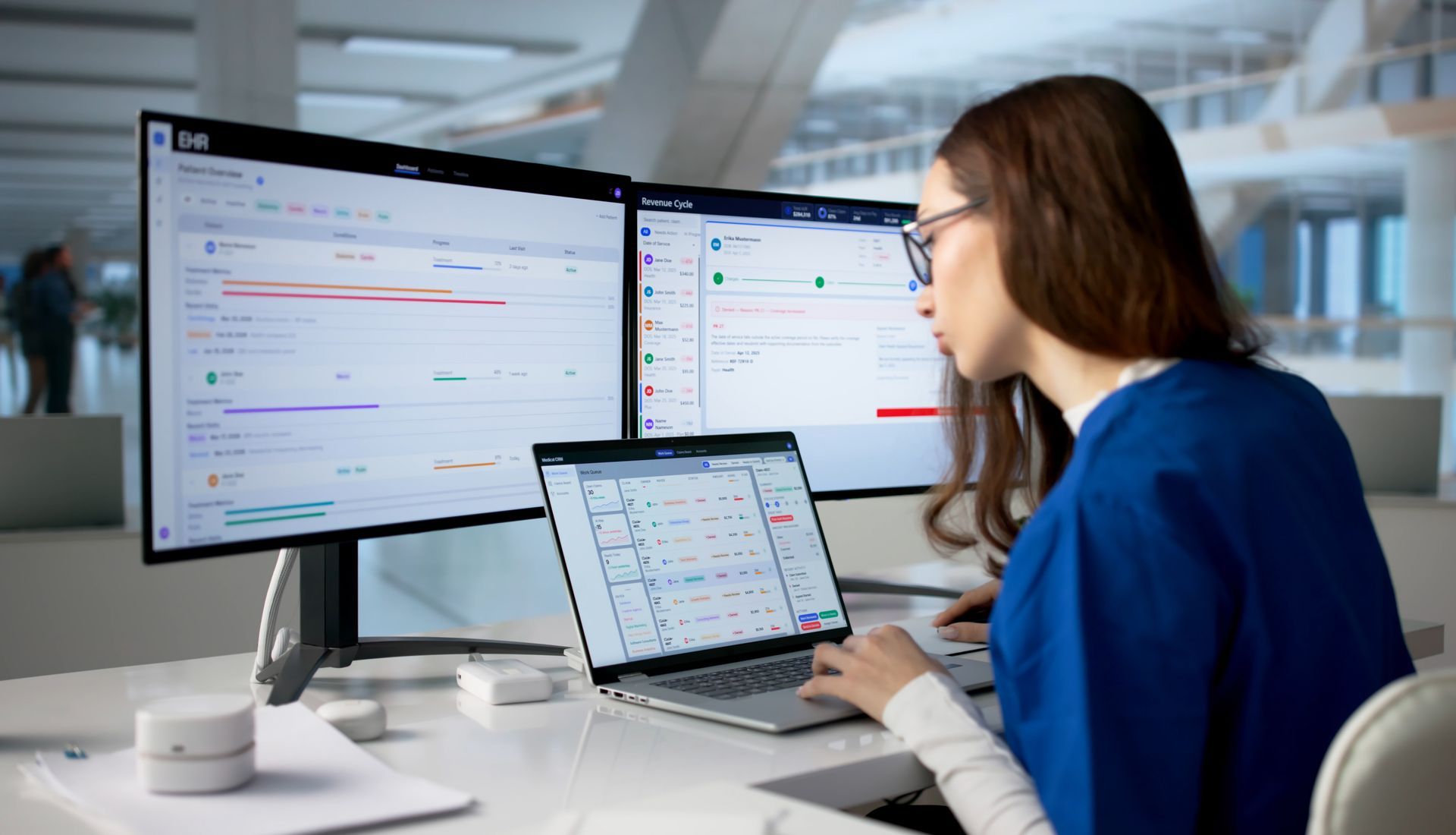 Person working at a desk with dual monitors and a laptop in a bright office