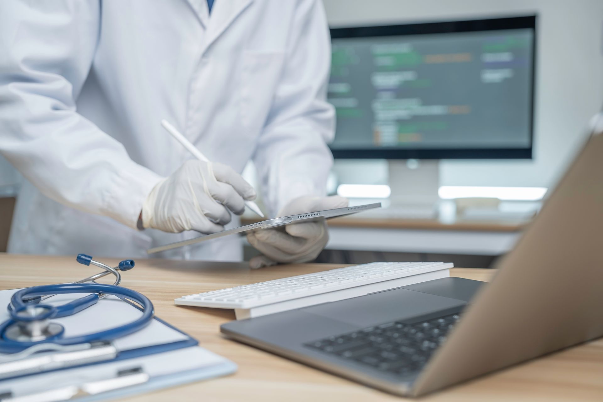 Doctor writing notes beside a laptop and stethoscope in a clinic office