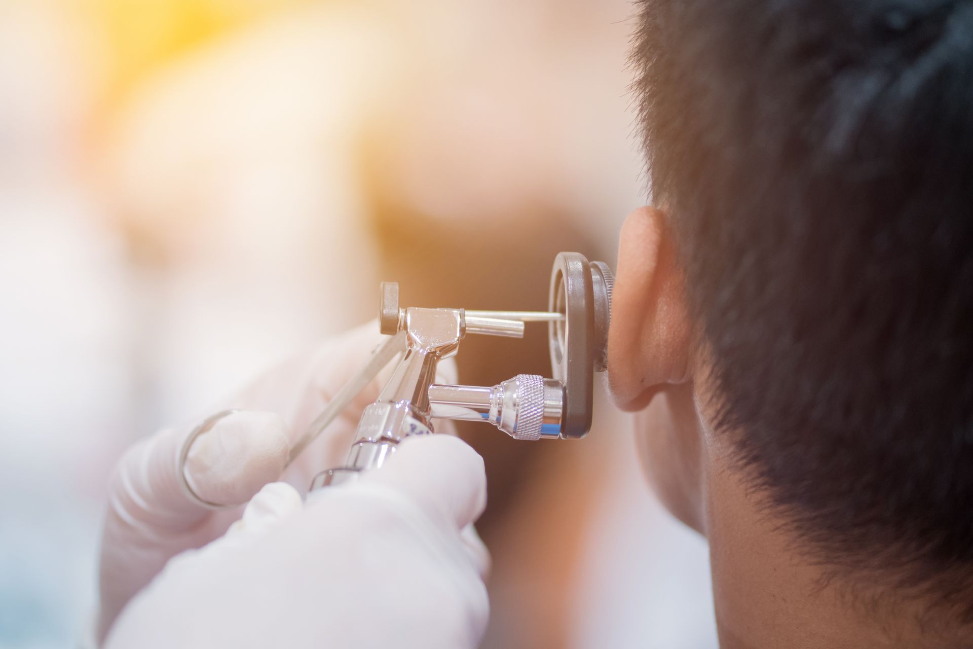 Ear being examined with an otoscope by gloved hands in a bright clinic setting