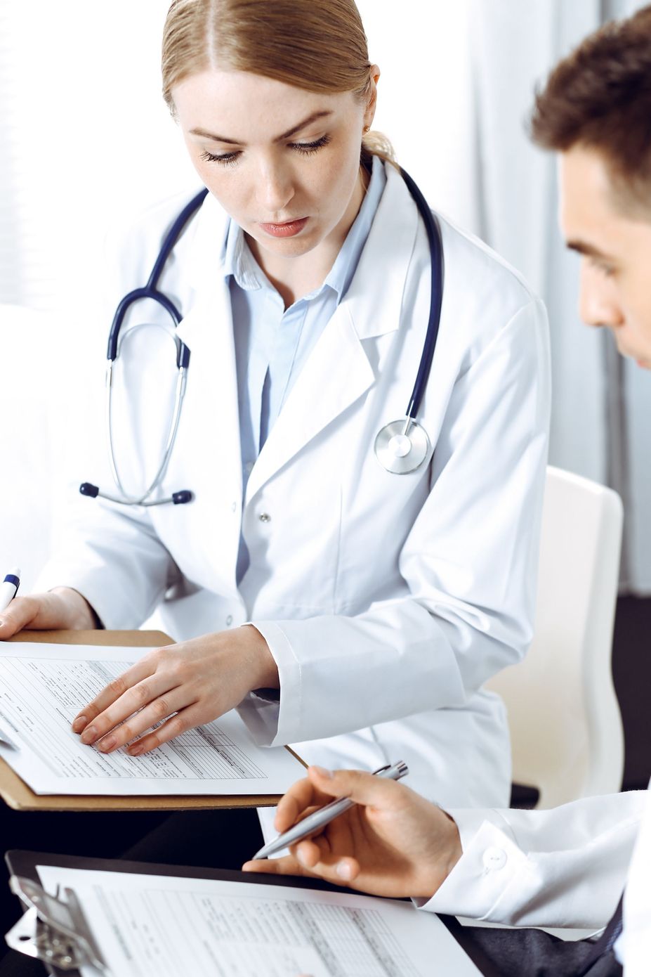 Doctor reviewing notes with a patient during a consultation, with a stethoscope visible.