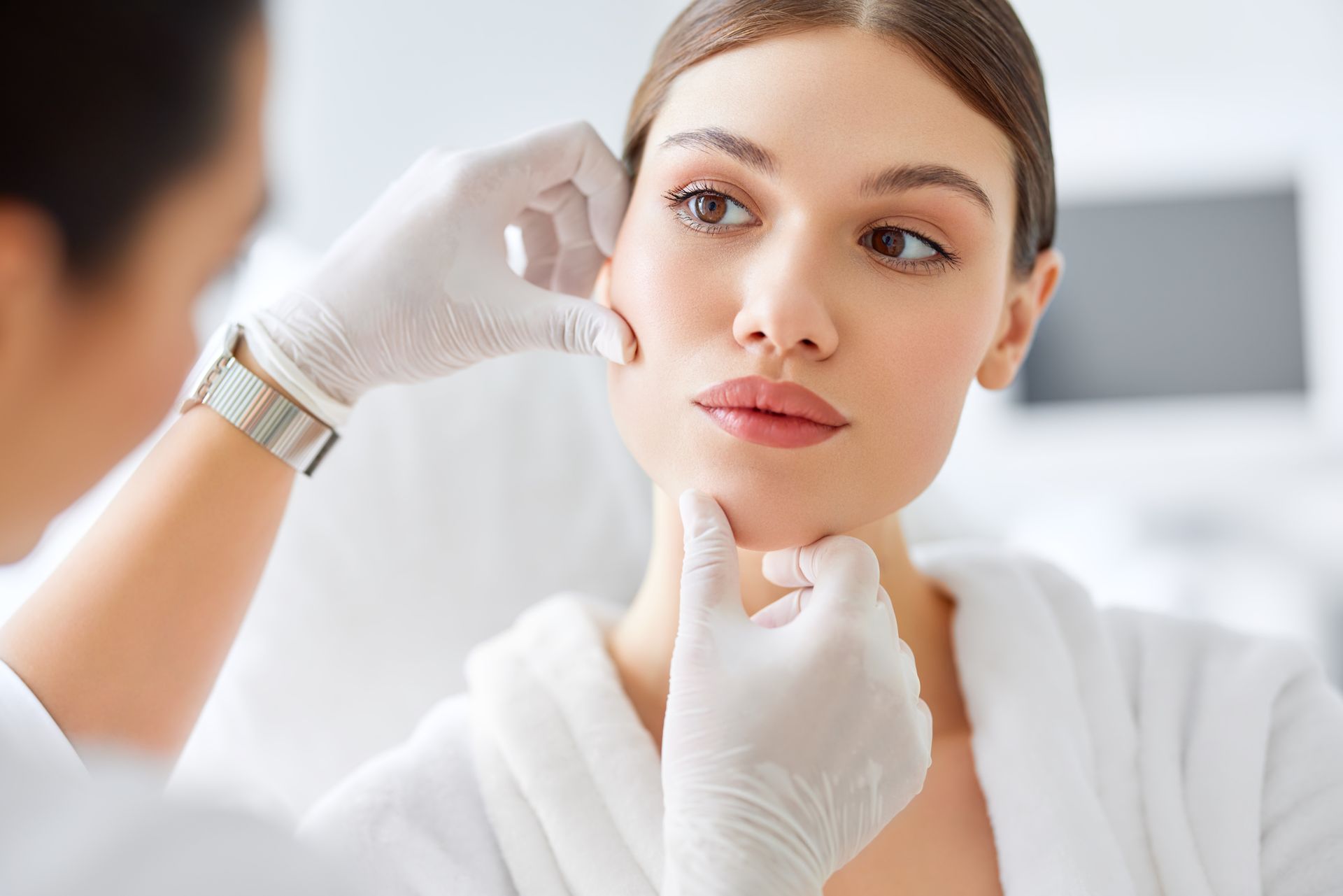 Gloved clinician examining a woman’s face in a bright spa or clinic setting