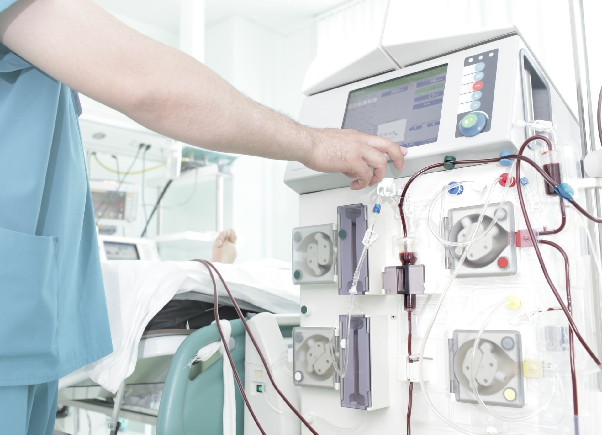 Nurse adjusting a dialysis machine beside a patient bed in a hospital room