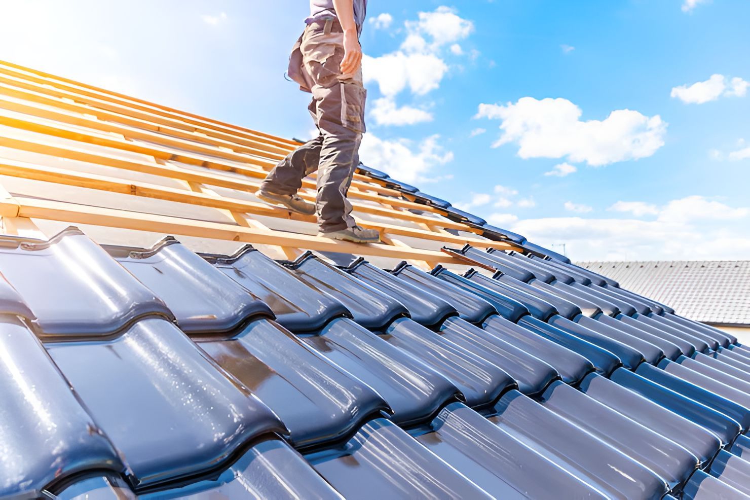 Worker installing blue roof tiles on a house under a bright sky