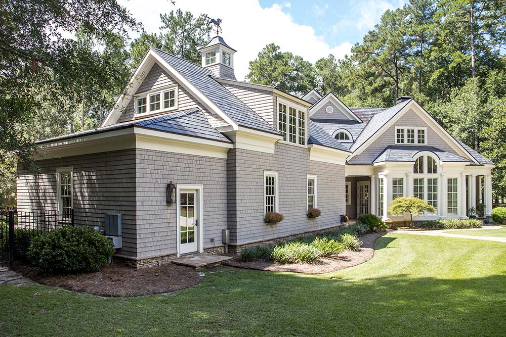 Large stone house with gabled roof and manicured lawn surrounded by trees
