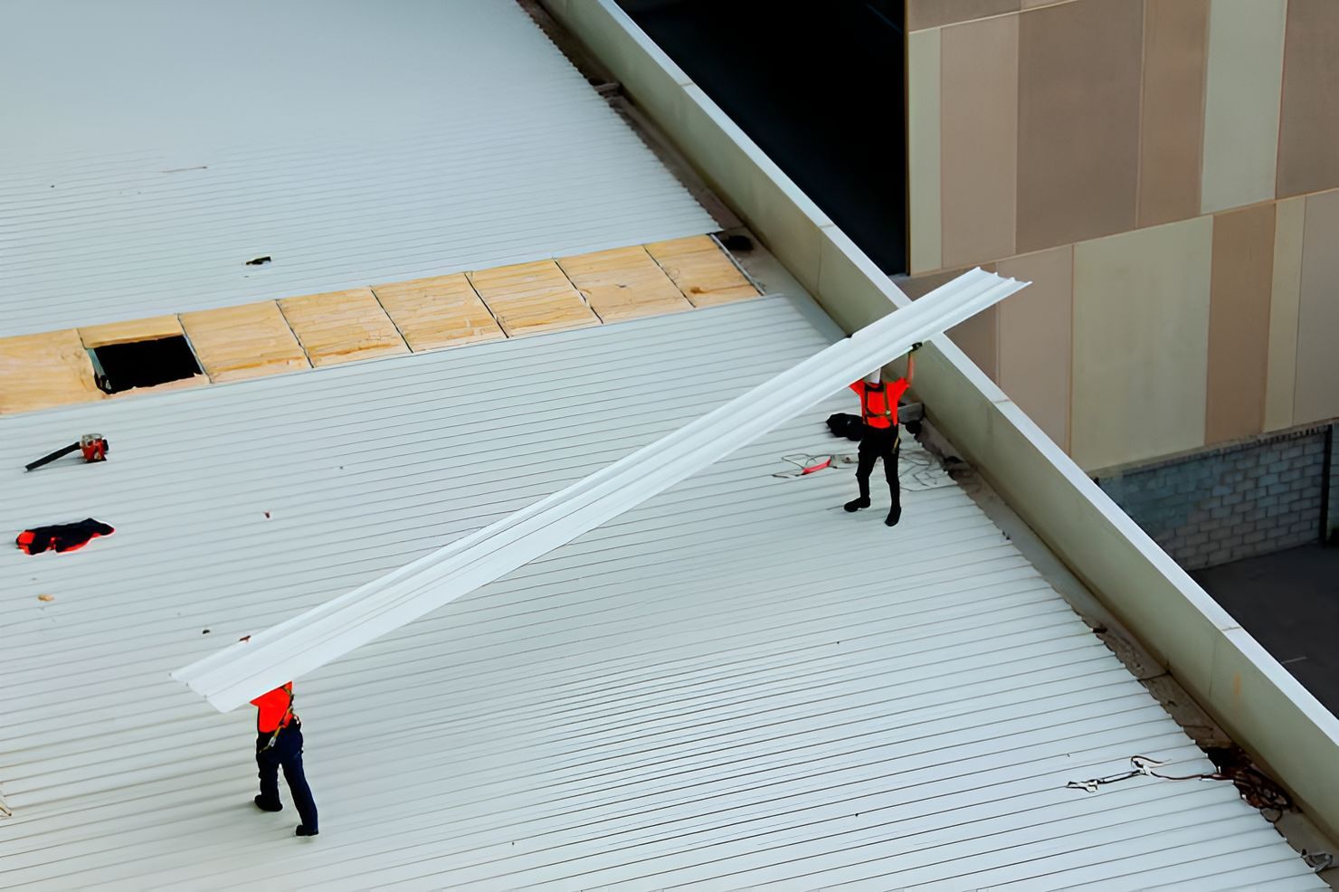 Workers in red vests on a white rooftop near a building wall