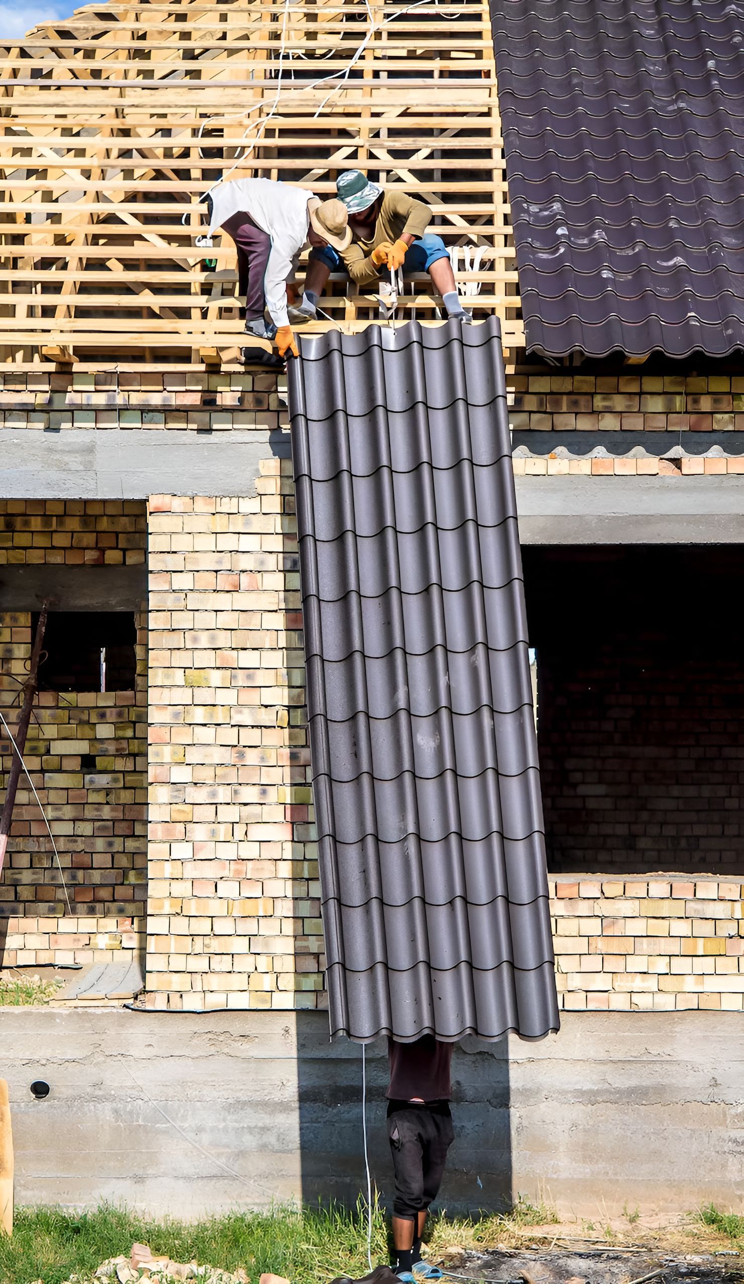 Workers lifting roof panels onto a brick building under construction